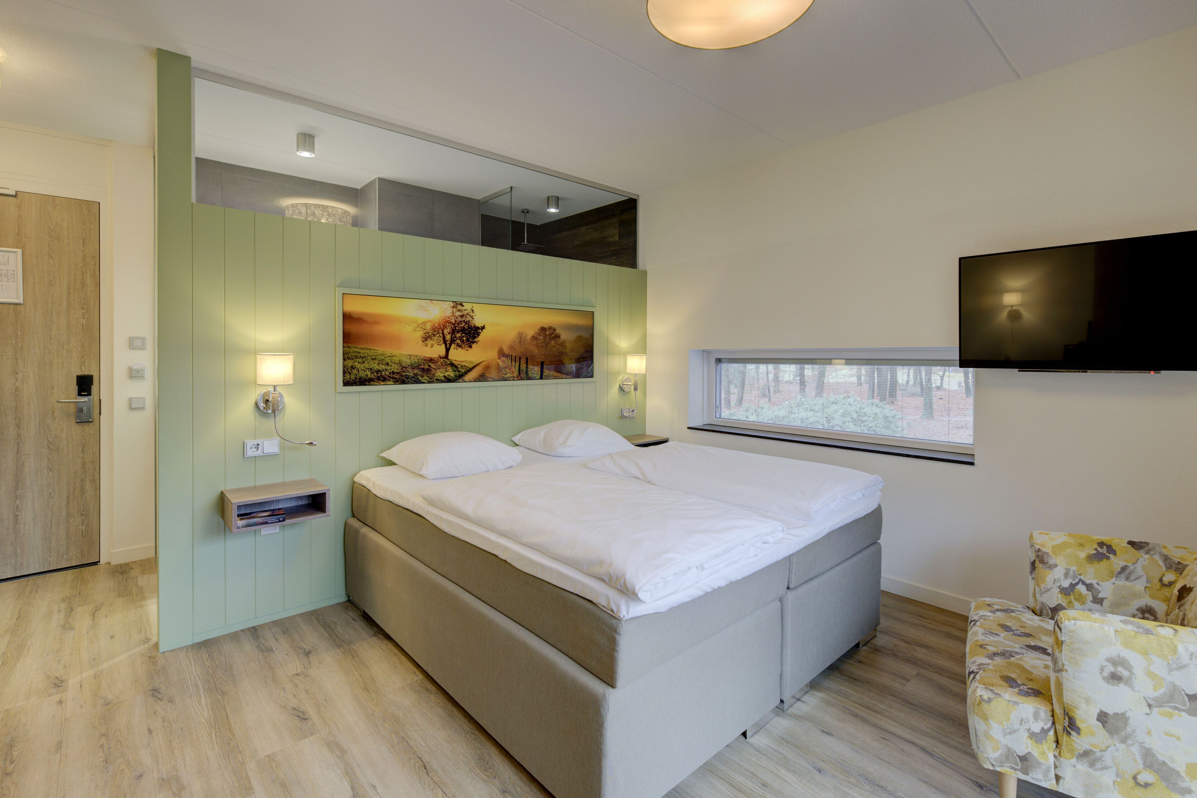Un dormitorio moderno con una cama grande, un televisor montado, un cuadro y una ventana.