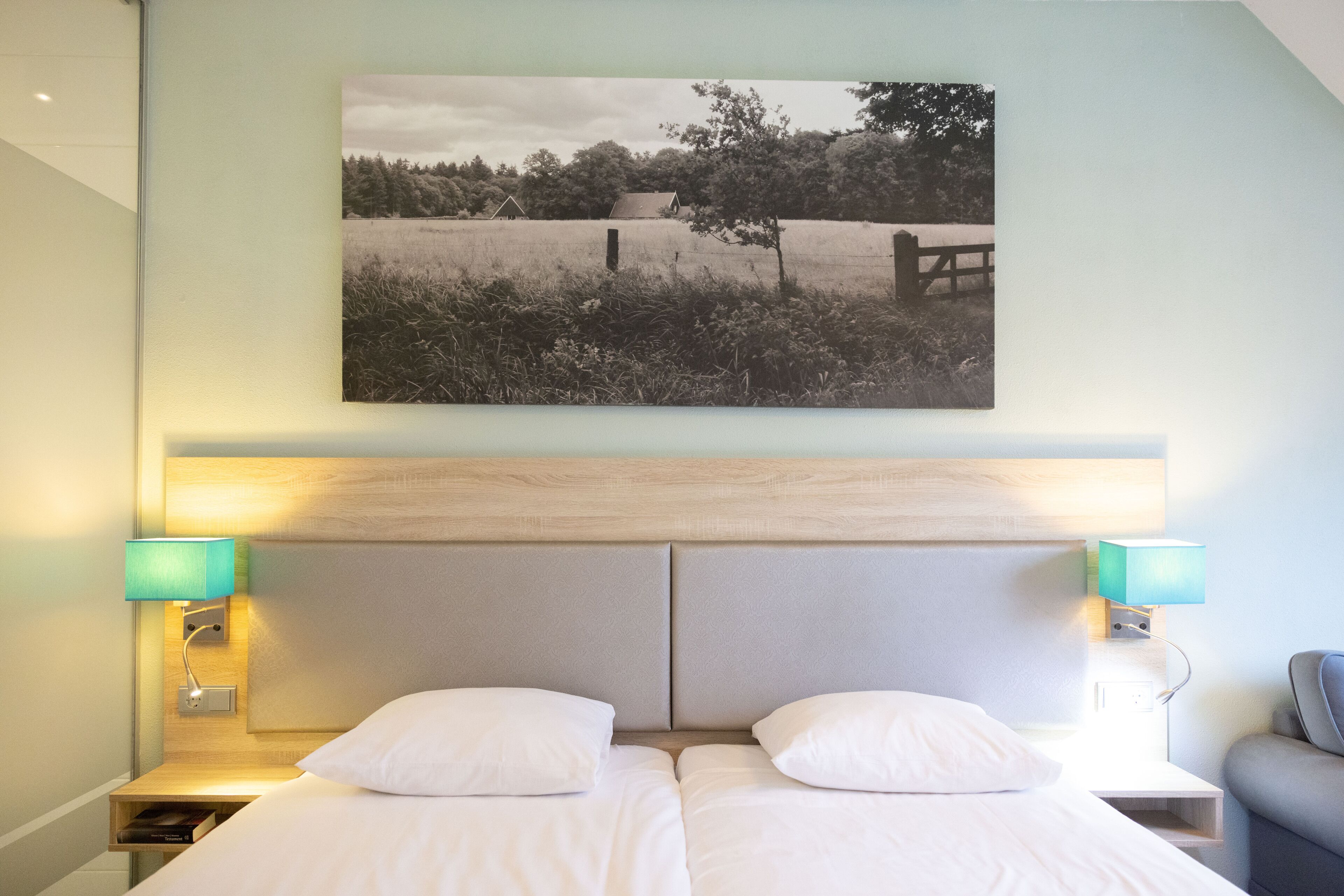 A double bed with two pillows, a wooden headboard, and two bedside lamps.