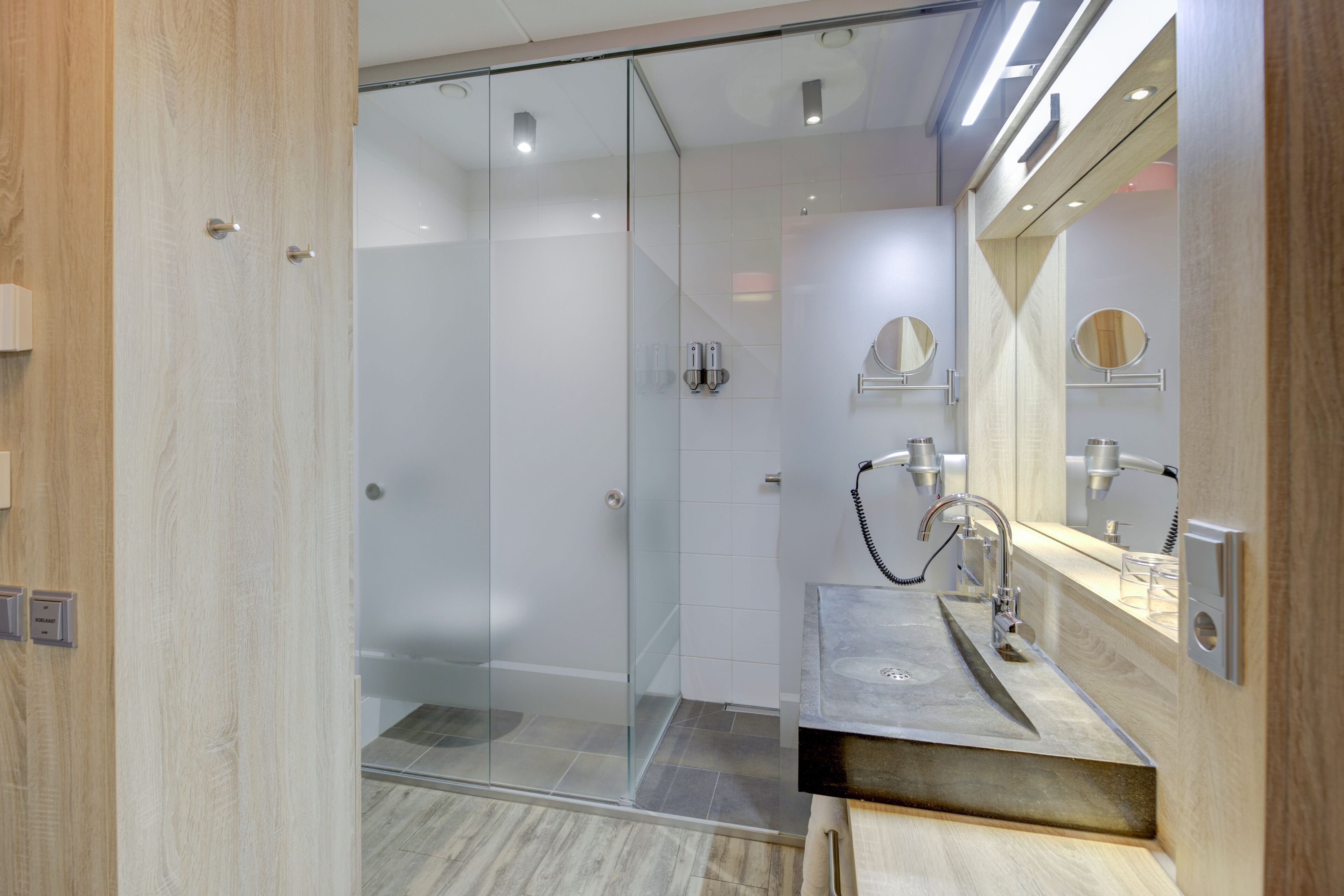 A modern bathroom with a glass shower enclosure, a sink with a mirror, and wooden accents.
