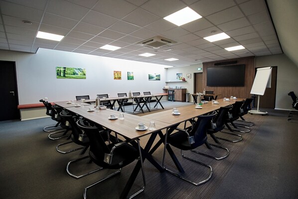 A conference room with a long table, chairs, a projector screen, and artwork on the walls.