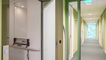 A corridor with doors, a control panel, and a view of a green outdoor area.
