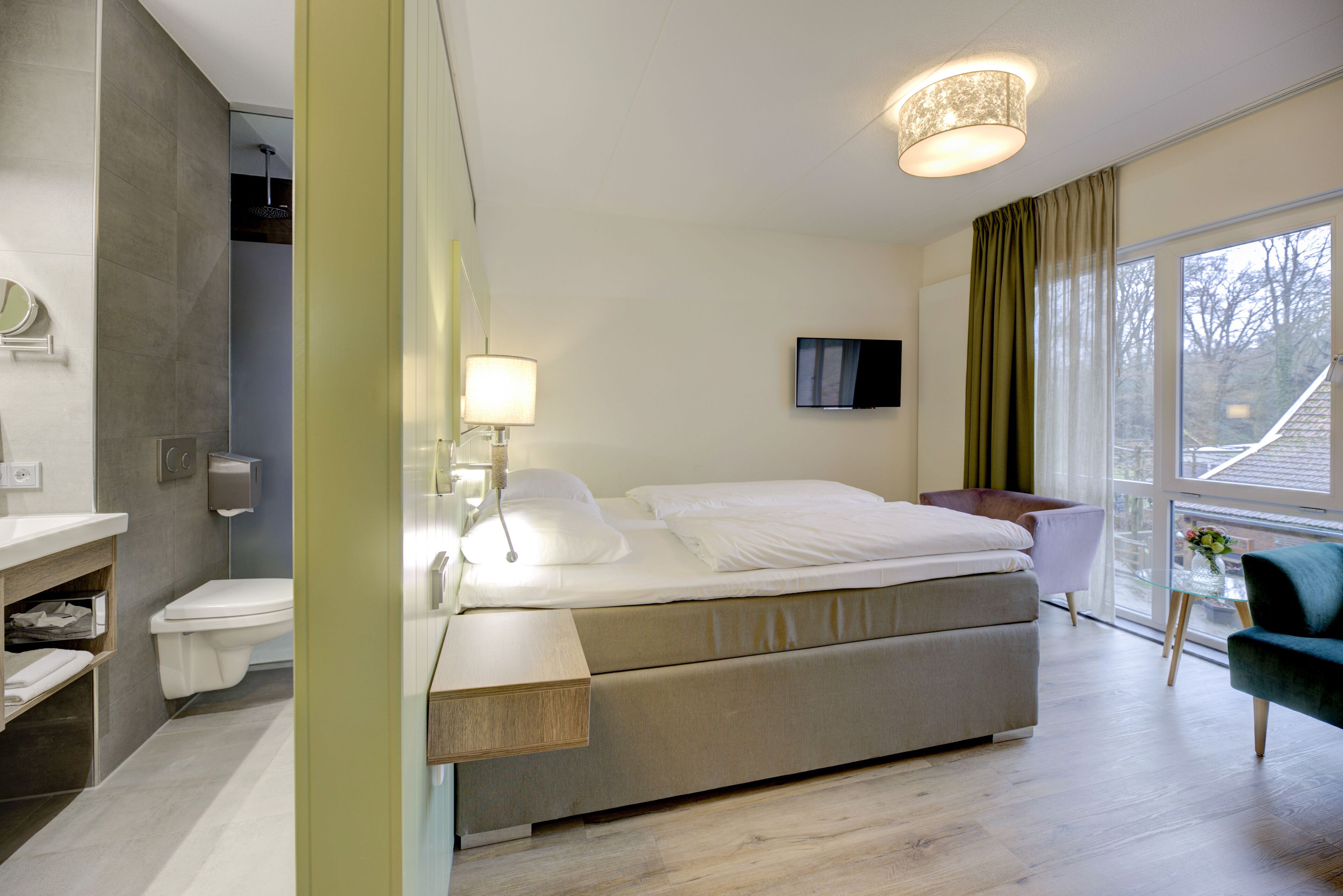 A modern bedroom with a bed, bedside table, lamp, and a view of the outside.