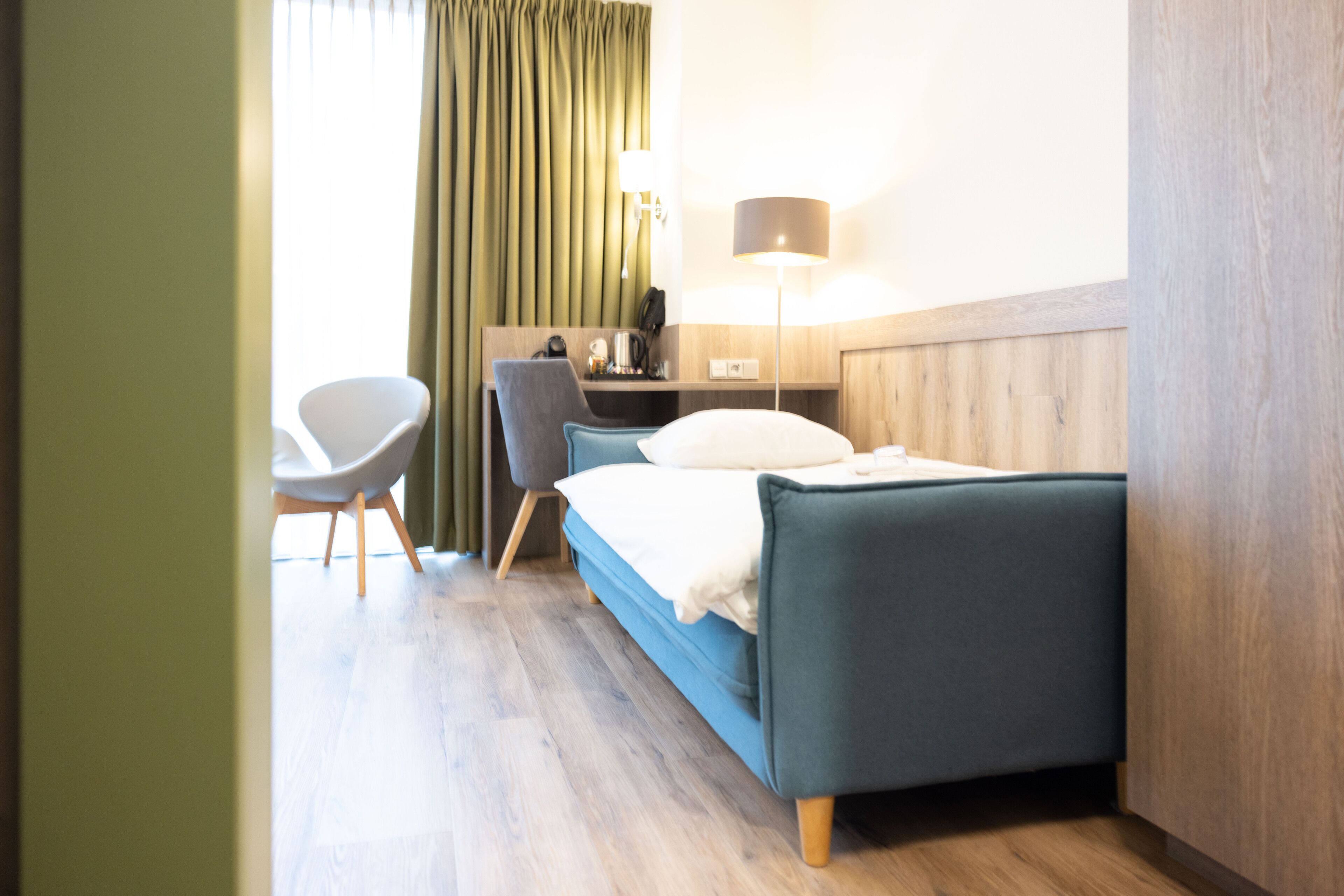A hotel room with a bed, a desk, a chair, a lamp, and a window with curtains.