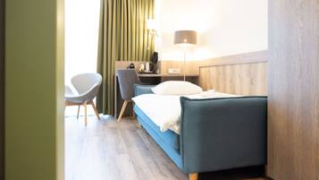 A hotel room with a bed, a desk, a chair, a lamp, and a window with curtains.