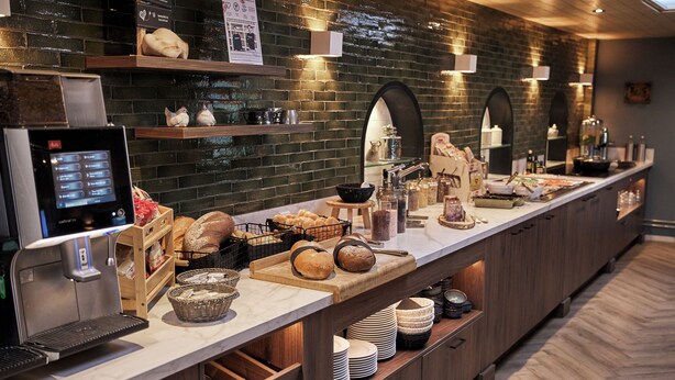 A buffet setup with a coffee machine, bread, and various food items. - Hotel Erve Hulsbeek (Oldenzaal)