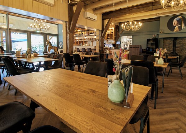 A restaurant interior with wooden tables and chairs, a green vase with flowers, and a chandelier.