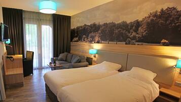 Habitación de hotel con una cama grande, un escritorio con silla, un televisor y un cuadro de un bosque en la pared.