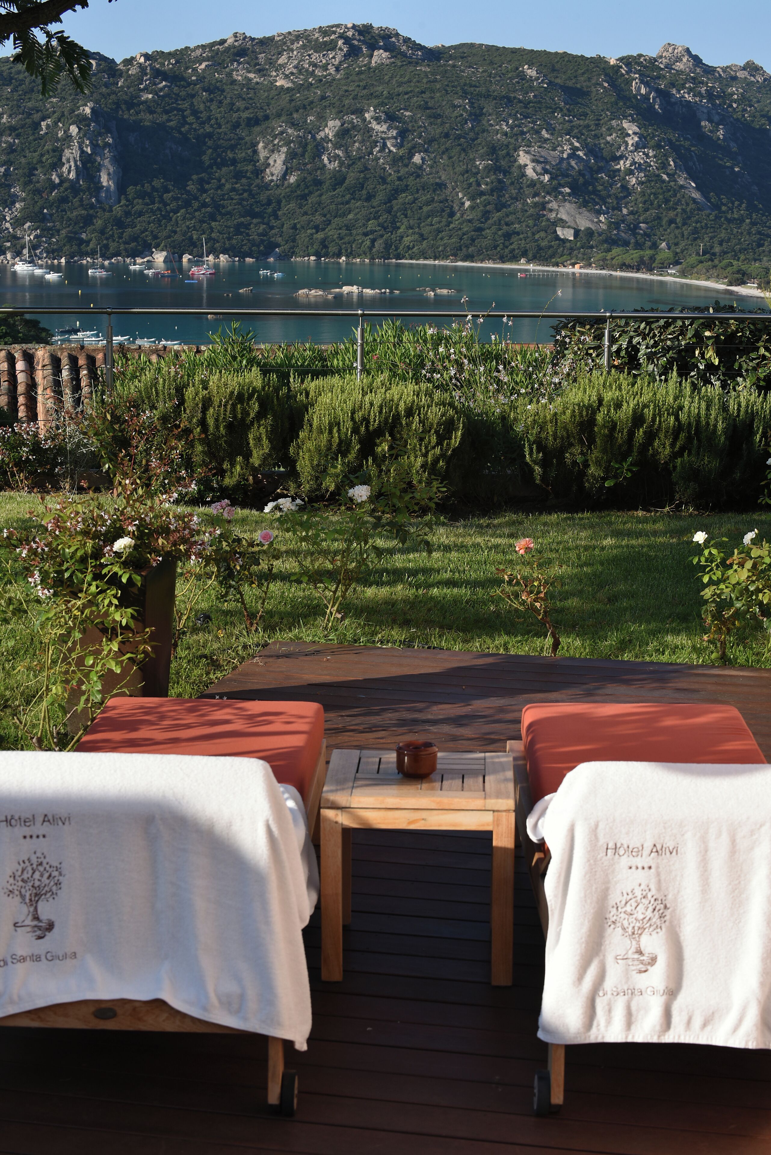 Una terraza con dos zonas de estar acolchadas, una mesa de madera y vistas a un lago y montañas.