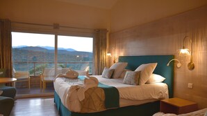A hotel room with a large bed, a balcony with chairs, and a view of the mountains. - Hôtel Alivi di Santa Giulia (Porto-Vecchio)