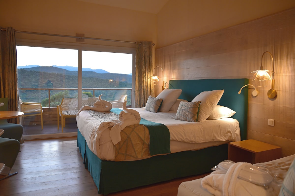 Una habitación de hotel con una cama grande, un balcón con sillas y vistas a las montañas.