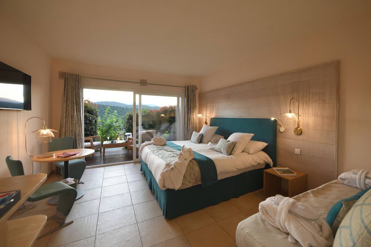 Una habitación de hotel con una cama grande, un balcón, un comedor y un televisor.