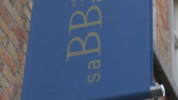 Une banderole bleue portant les inscriptions « ed & breakfast » et « BB Bajon », fixée sur un support métallique contre un mur de briques.
