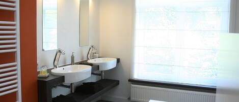 Un baño moderno con dos lavamanos, una bañera grande y una ventana con persianas.