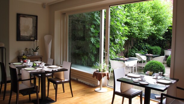 Comedor con mesas y sillas, ventanas amplias y vistas al exterior con vegetación.