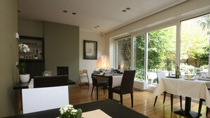 Un comedor con una mesa lista para dos personas, una planta en maceta y un cuadro en la pared.