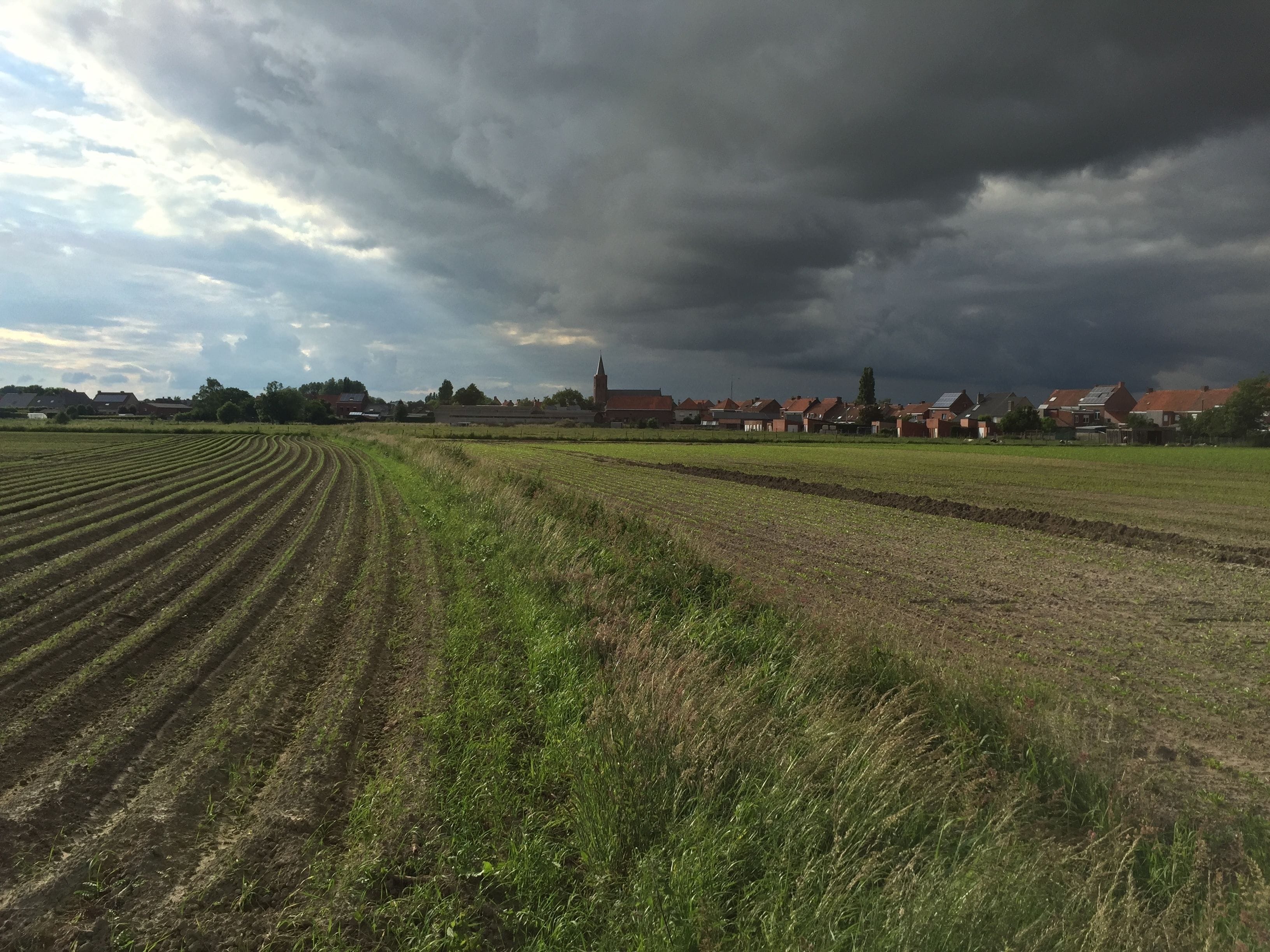 A rural landscape with fields and houses under a cloudy sky.