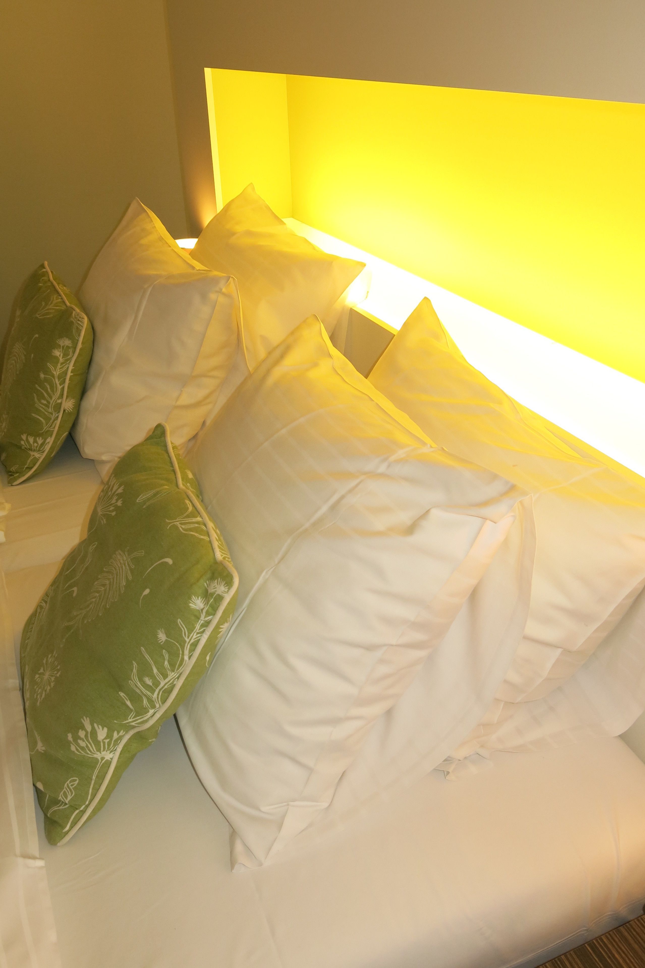A bed with white bedding and green patterned pillows.
