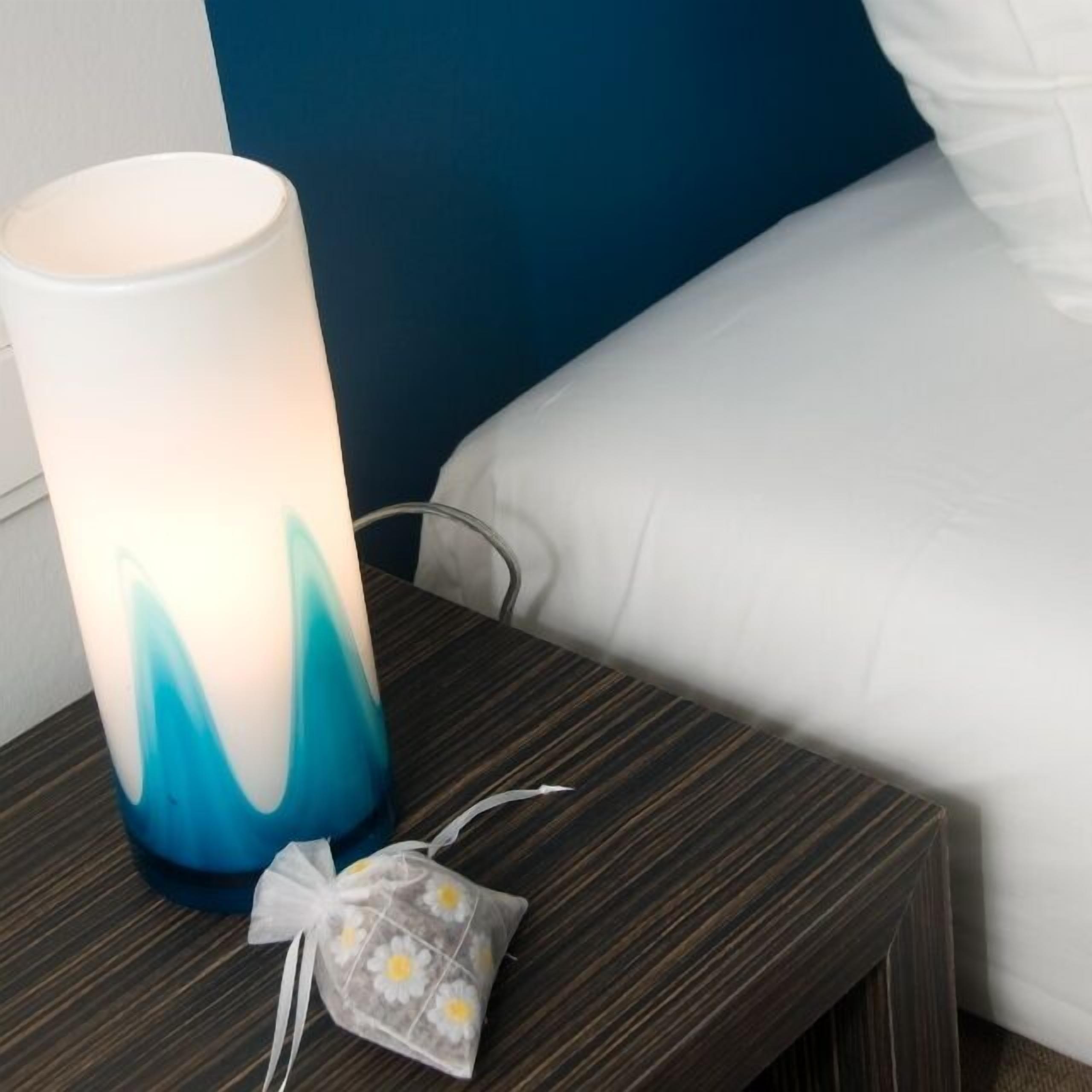 A bedside table with a lamp, a power cord, and a small gift bag with a floral design.