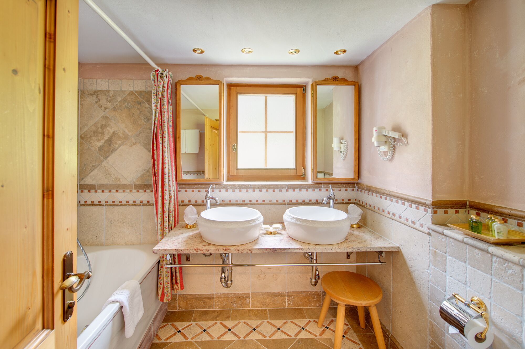 Ein Badezimmer mit zwei Waschbecken, einer Badewanne, einer Duschvorhang und einem hölzernen Hocker.