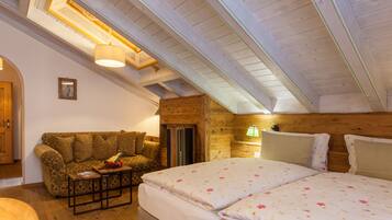 A cozy room with a wooden ceiling, a bed with floral bedding, a sofa with a fruit basket, and a small table.