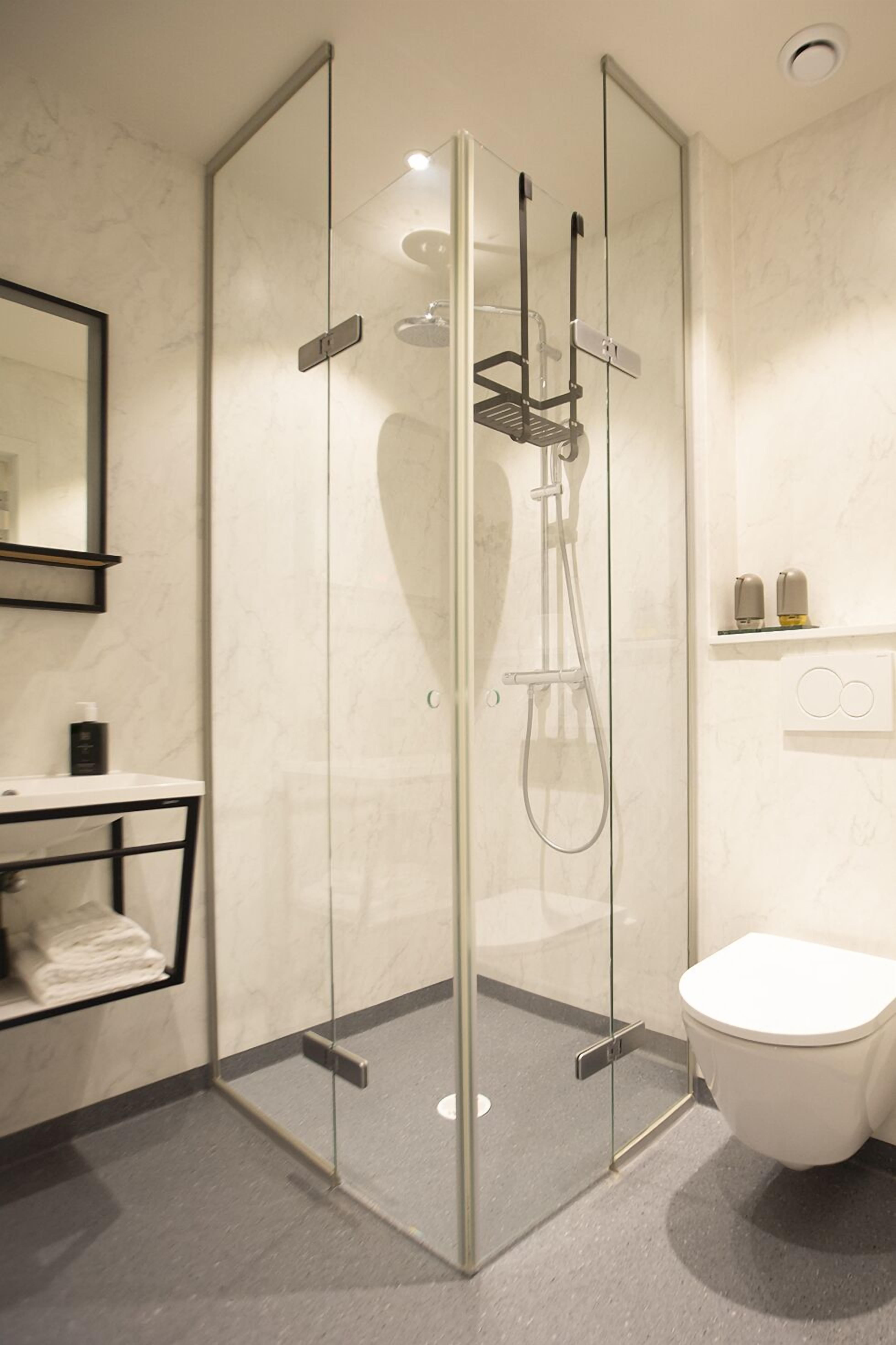 Un baño moderno con ducha envuelta en cristal, inodoro blanco y pared de azulejos de mármol.