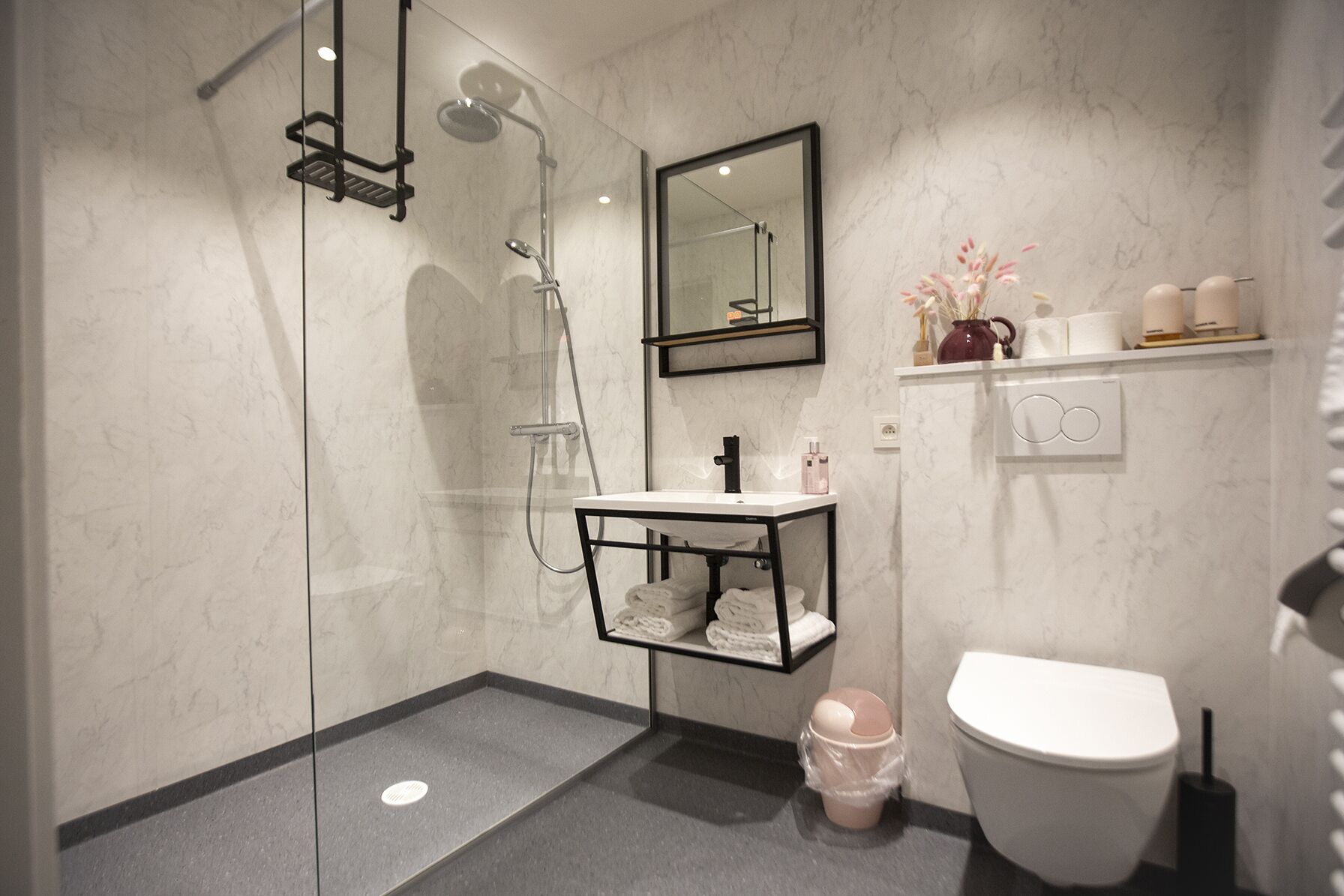 A modern bathroom with a glass-enclosed shower, a black-framed sink, a white toilet, and a marble wall.
