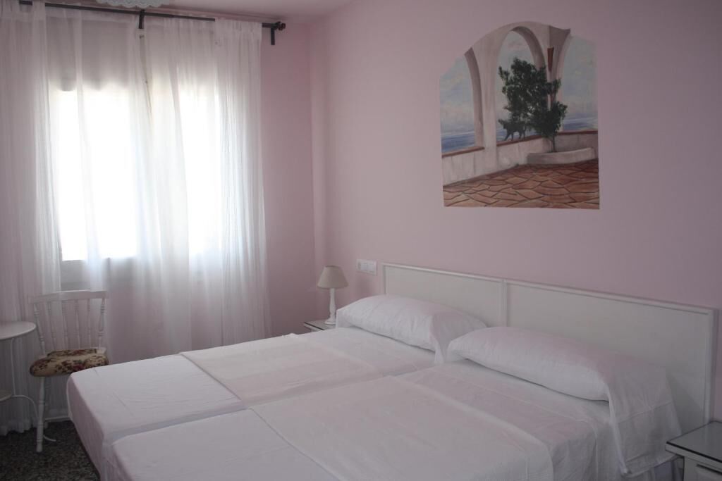A room with two beds, a chair, a lamp, and a painting on the wall.