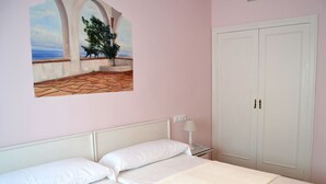A bedroom with a bed, a nightstand, a lamp, a wardrobe, and a painting of a coastal scene. - Hostal Isabel II (Figueres)