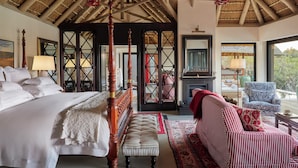 A bedroom with a large bed, a bench, a sofa, a fireplace, and a view through a glass door. - Royal Malewane (Hoedspruit)