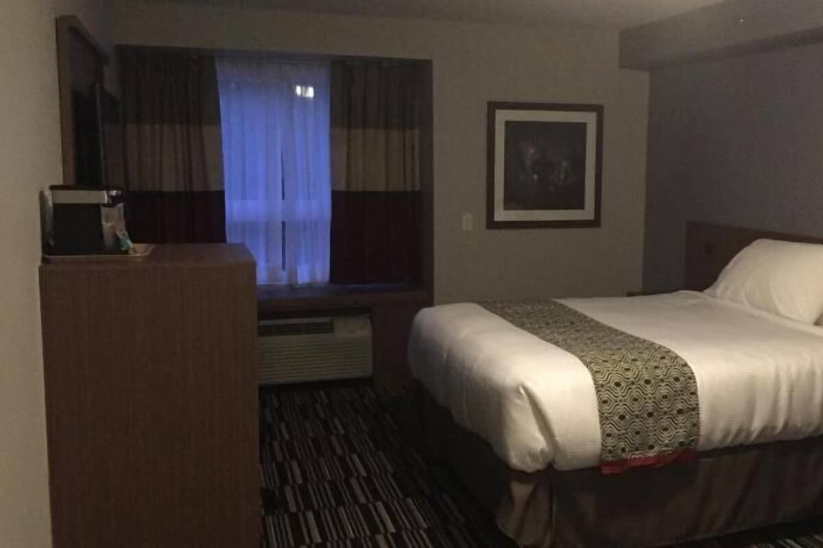 A hotel room with a bed, a desk, a window with curtains, and a framed picture on the wall.