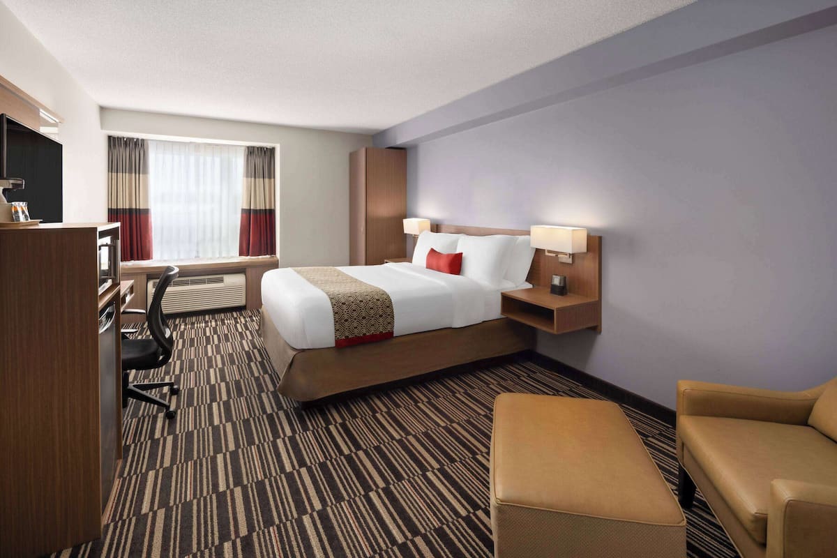A hotel room with a bed, a desk, a chair, a sofa, and a TV.