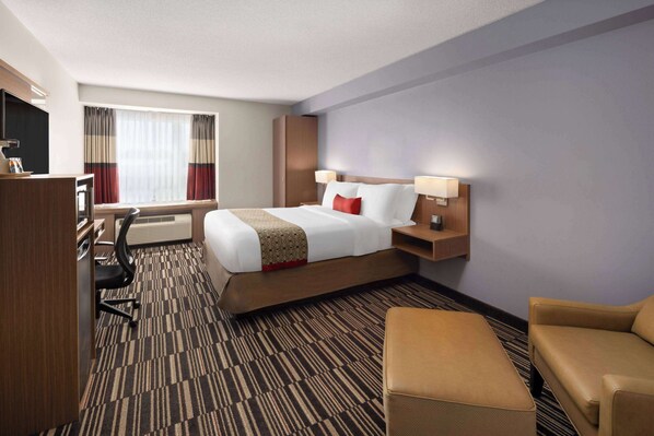 A hotel room with a bed, a desk, a chair, a sofa, and a TV.