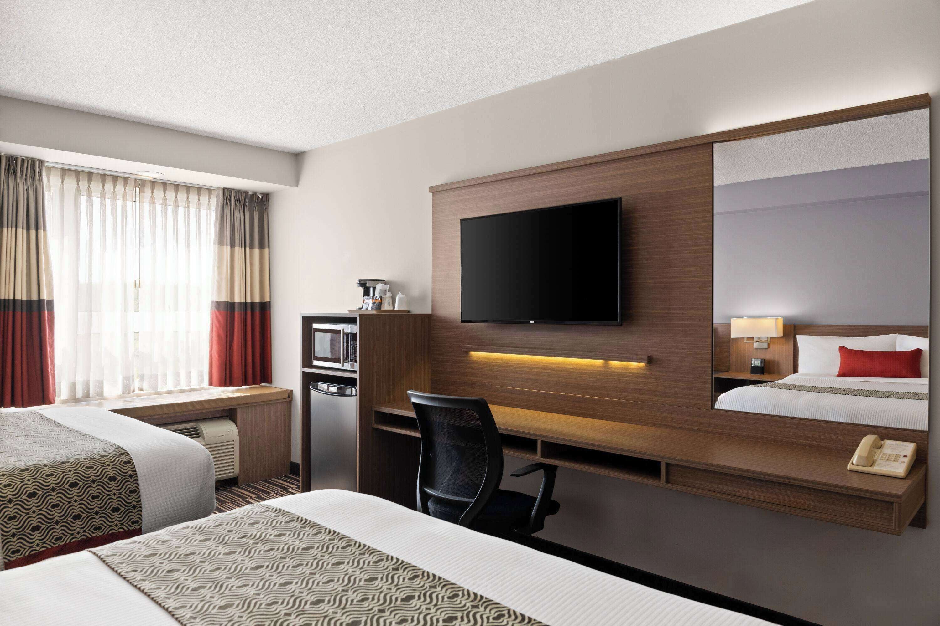 A hotel room with two beds, a desk, a television mounted on the wall, and a mirror reflecting the bed.