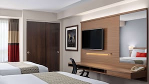 Una habitación de hotel con dos camas, un escritorio, una silla, un televisor y un teléfono.