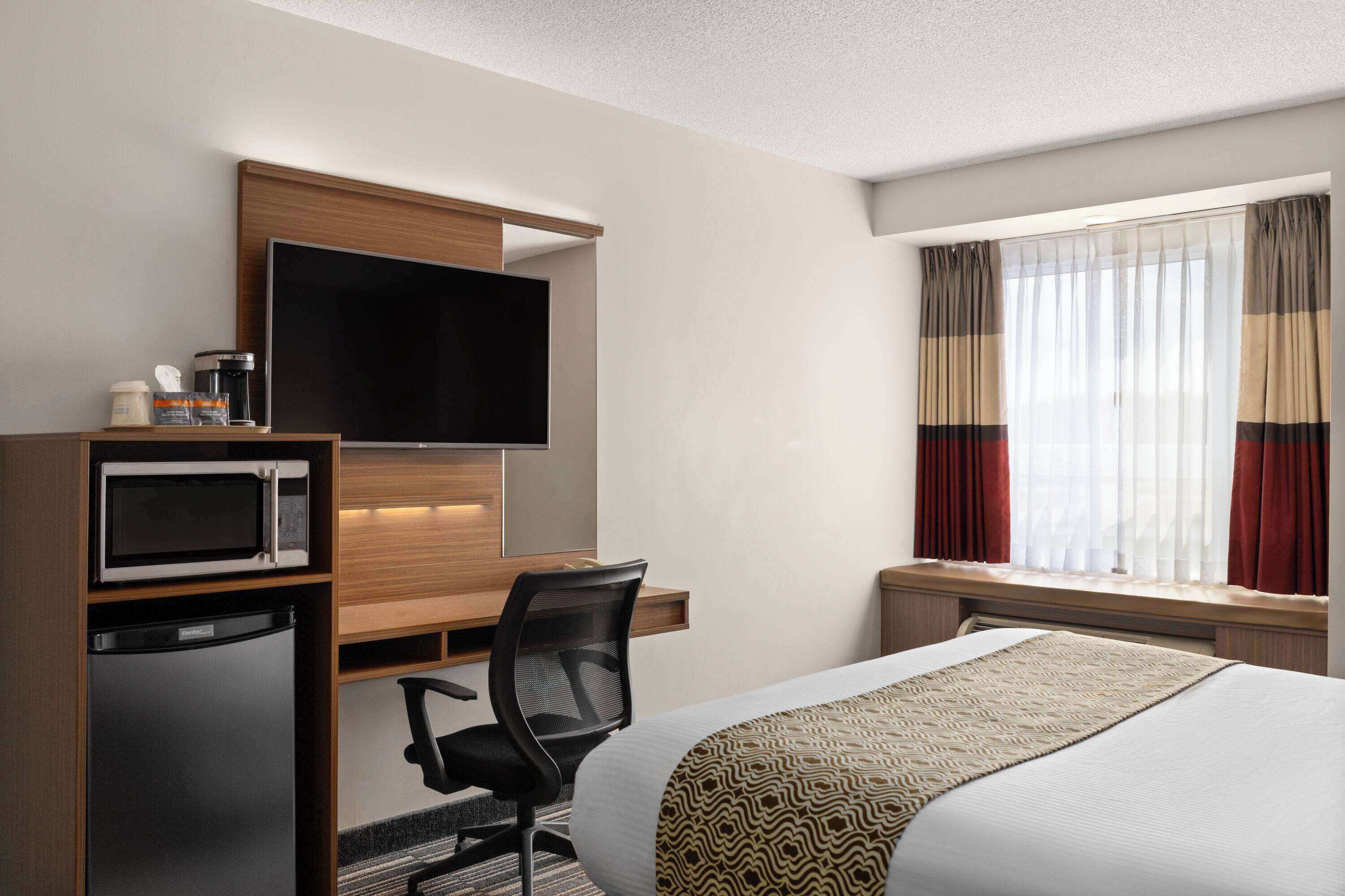 A hotel room with a bed, a desk with a computer, a television, a microwave, and a refrigerator.
