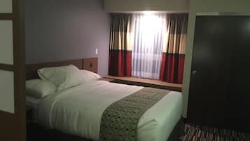 A hotel room with a bed, a window with curtains, a door, and a carpeted floor.