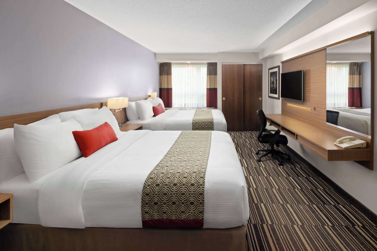 A hotel room with two beds, a desk, a chair, a TV, and a mirror.