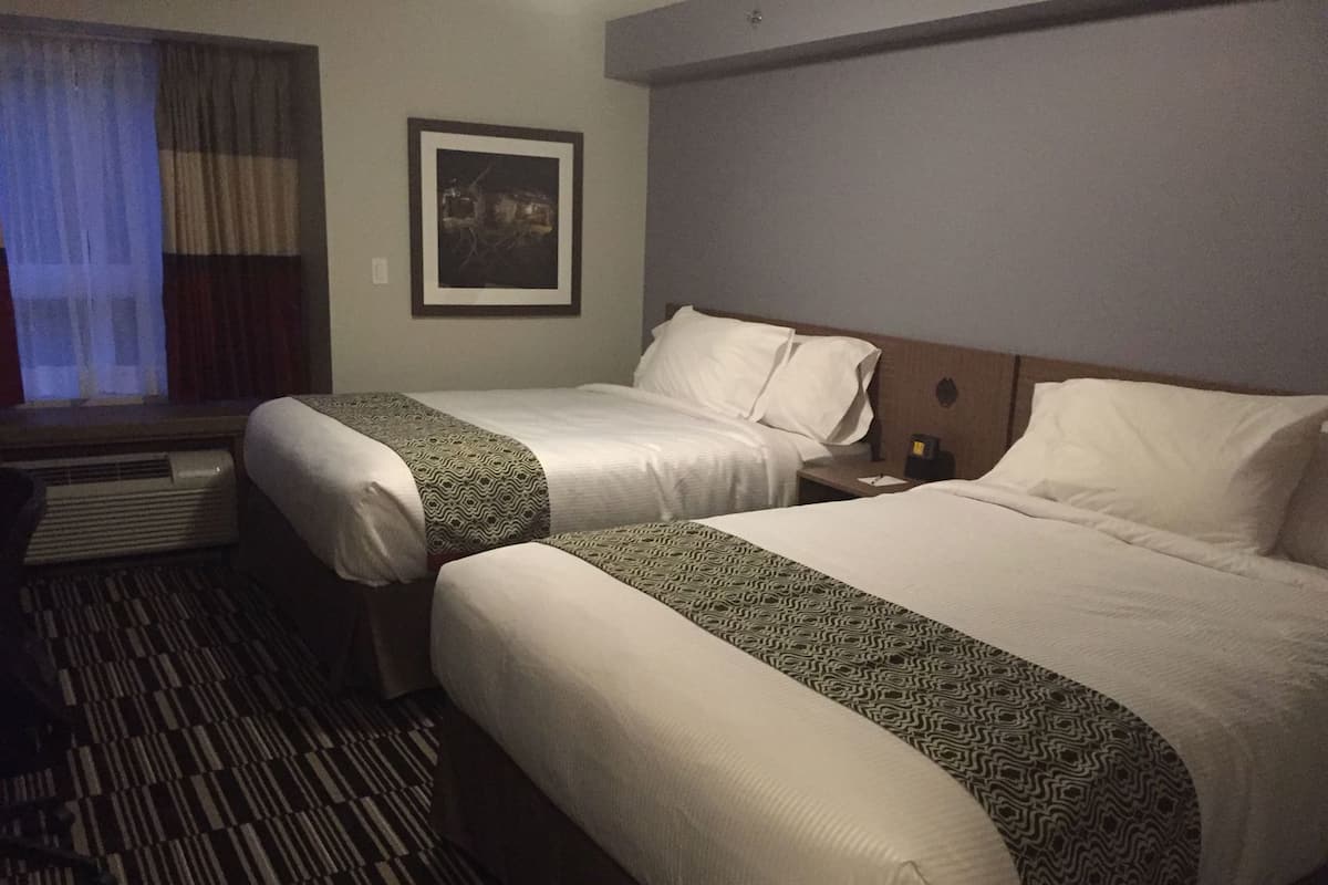 A hotel room with two beds, a window with curtains, a framed picture on the wall, and a patterned carpet.