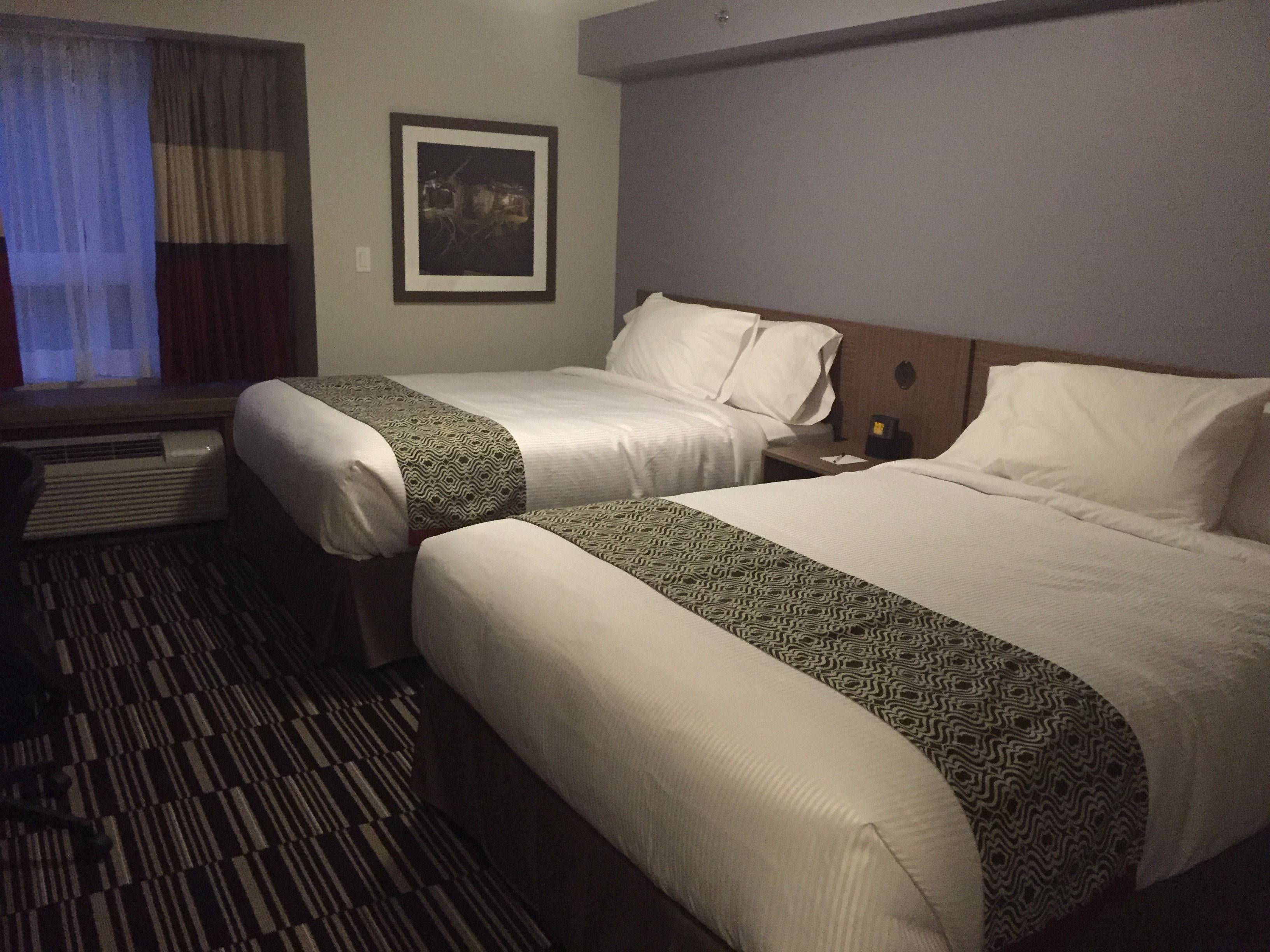 Habitación de hotel con dos camas, una ventana con cortinas, un cuadro enmarcado en la pared y una alfombra estampada.
