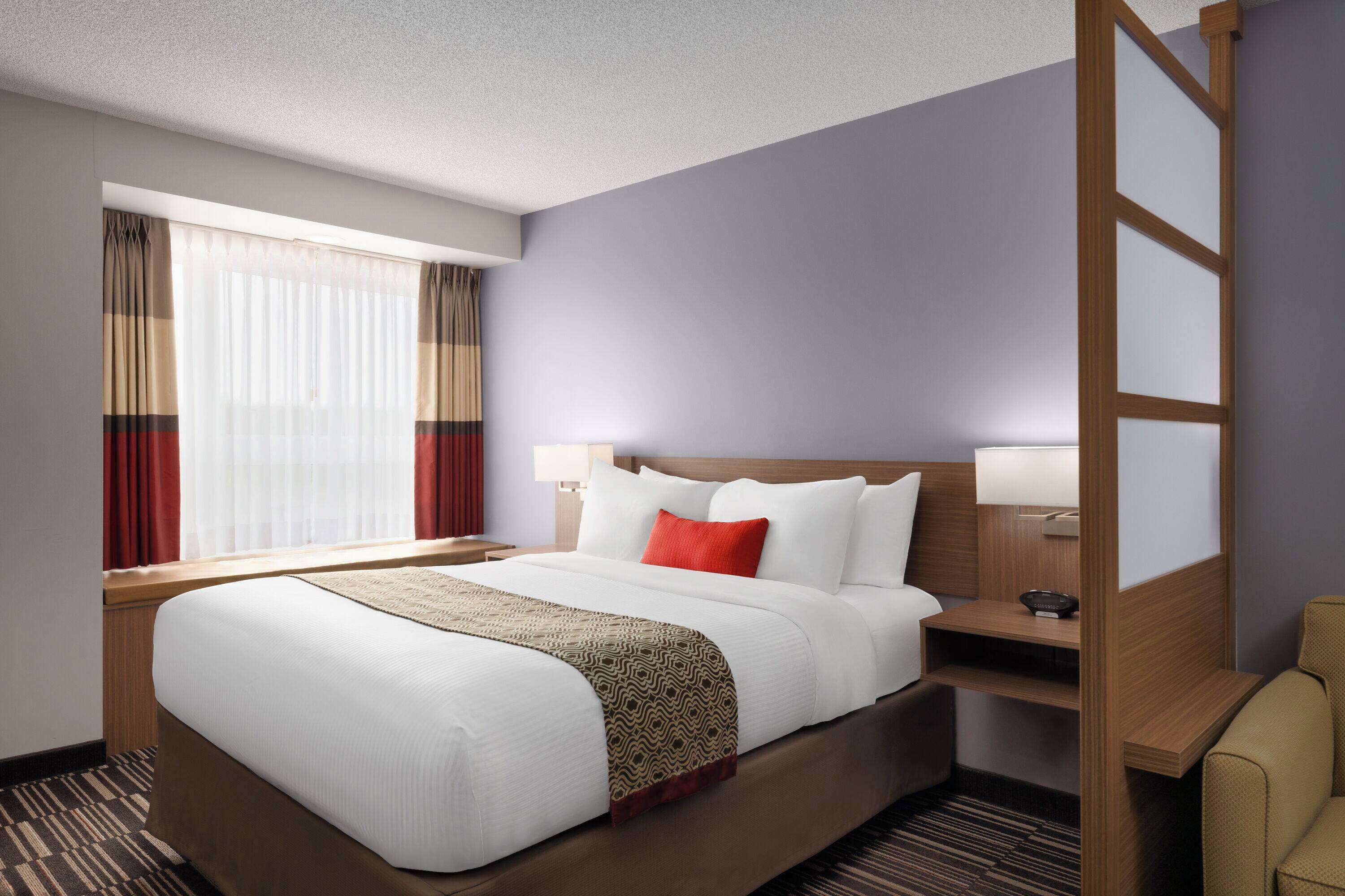 A hotel room with a large bed, a bedside table, a chair, and a window with curtains.