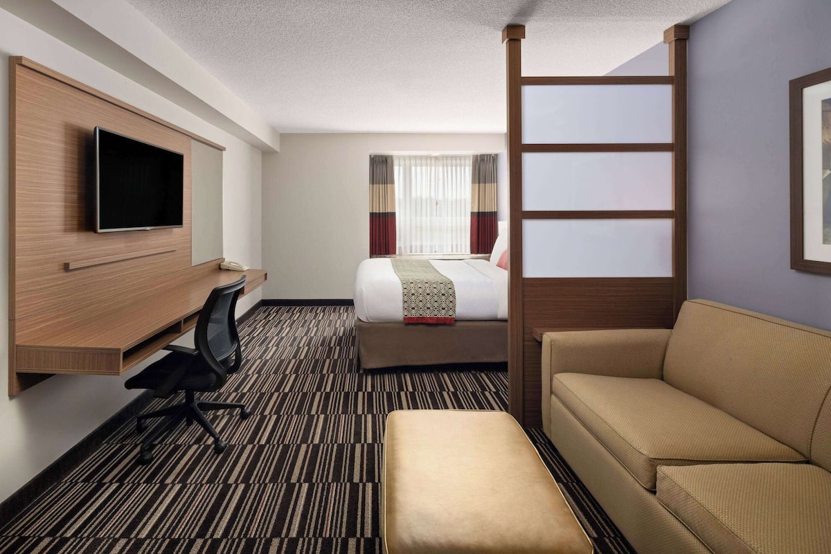 A hotel room with a bed, a sofa, a desk with a chair, a television, and a window with curtains.