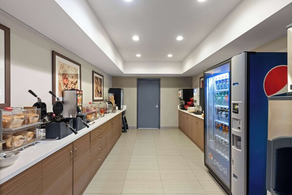 Una cocina de hotel con una zona de bufé, un refrigerador de Pepsi y una puerta al fondo.