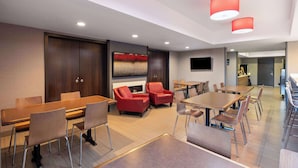 Un moderno vestíbulo de hotel con un largo mostrador de recepción de madera, sillones de cuero rojo y un televisor de pantalla plana grande montado en la pared.