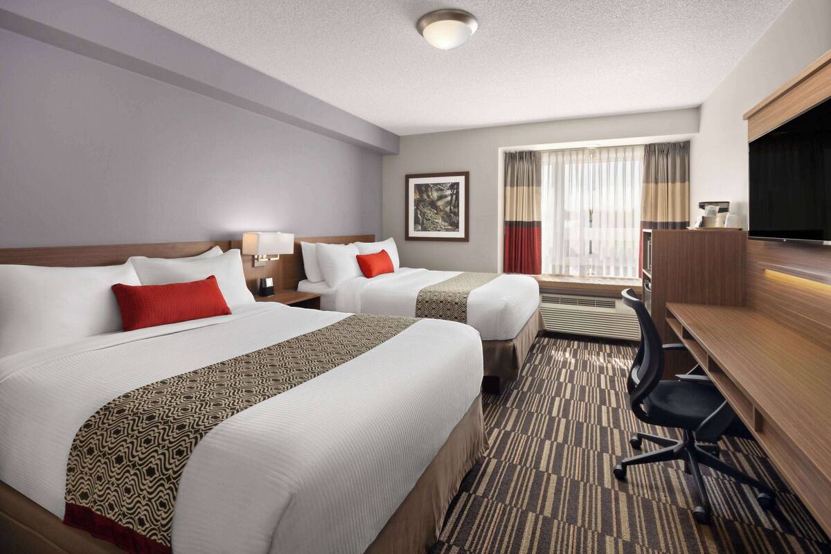 A hotel room with two beds, a desk, a chair, a television, and a window with curtains.