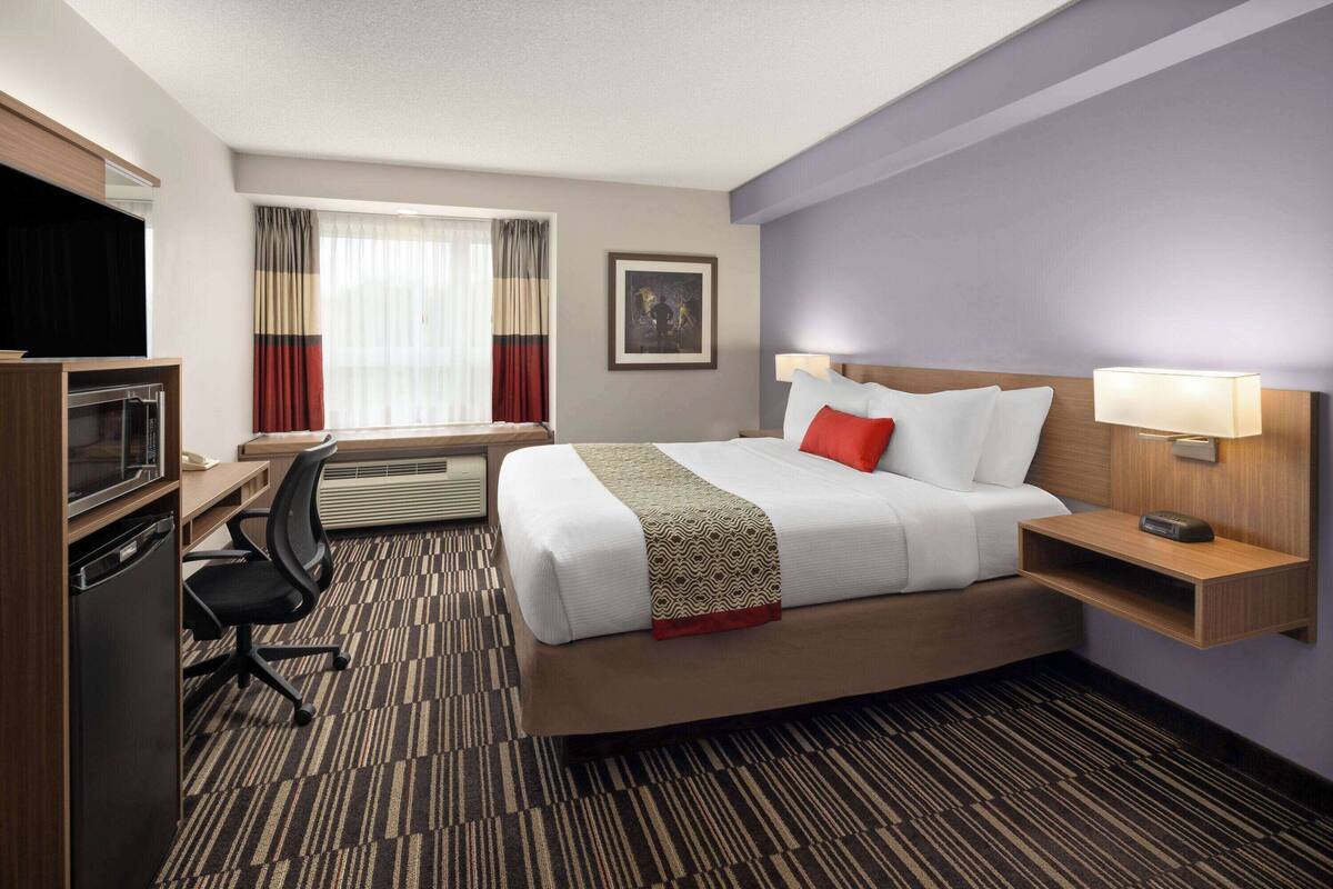 A hotel room with a bed, desk, chair, TV, and a window with curtains.