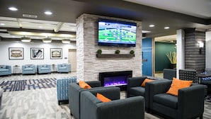 A modern lounge area with a flat-screen TV mounted on a stone wall, a fireplace, and several sofas with orange cushions. - Western Star All Suites Signature Hotel (Estevan)