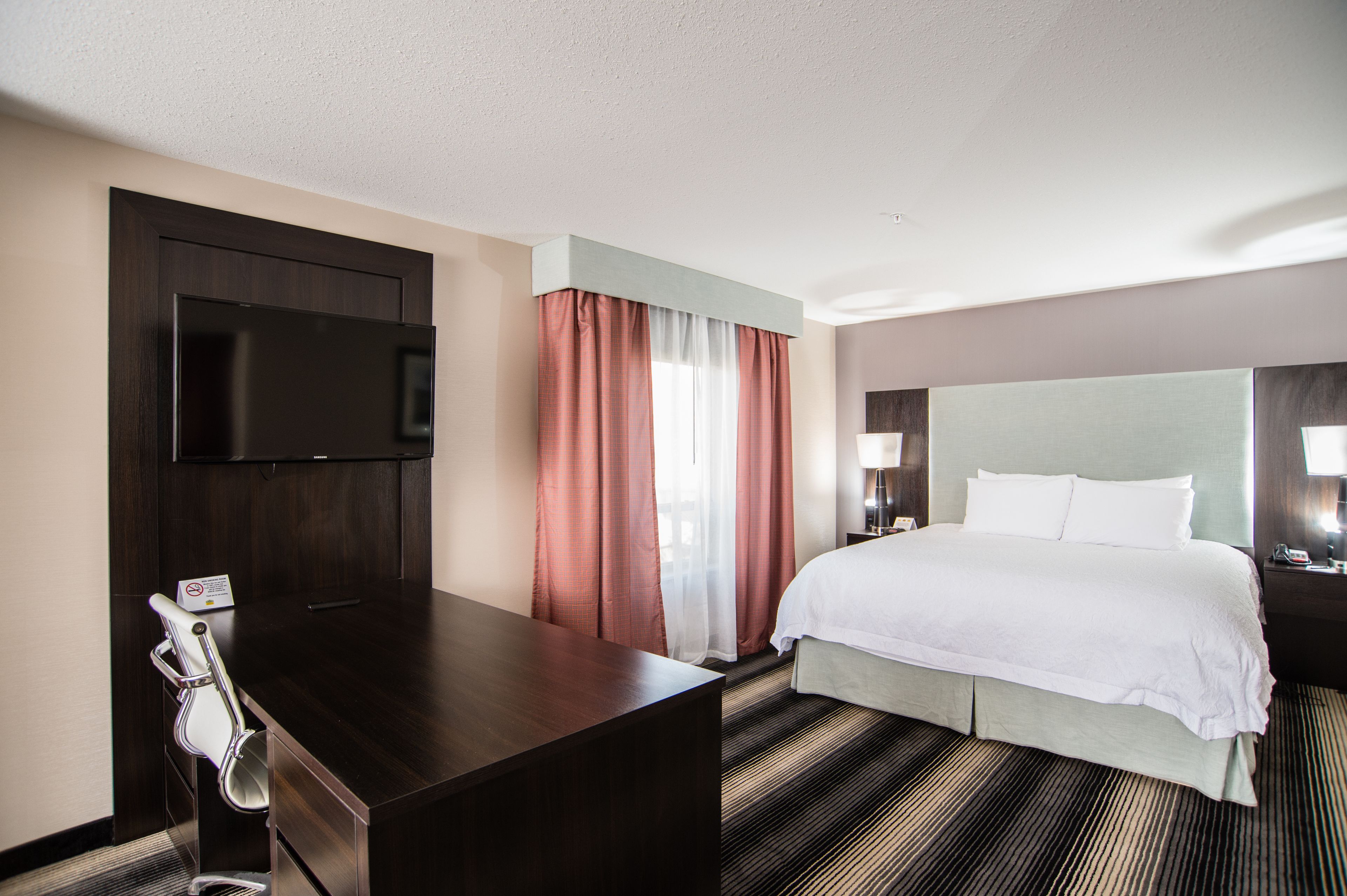 Une chambre d’hôtel avec un lit, un bureau, une télévision et une fenêtre avec des rideaux.