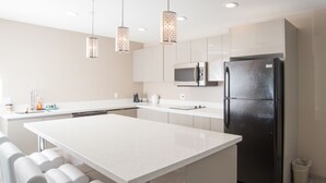 A modern kitchen with a central island, stainless steel appliances, and pendant lighting. - Western Star All Suites Signature Hotel (Estevan)