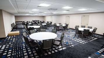 Un salón de conferencias con varias mesas y sillas, suelo alfombrado e iluminación empotrada en el techo.
