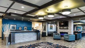 A hotel lobby with a reception desk, seating area, fireplace, and a large TV screen. - Western Star All Suites Signature Hotel (Estevan)